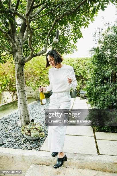 woman walking down stairs with bottle of wine and glasses for backyard party - white pants foto e immagini stock