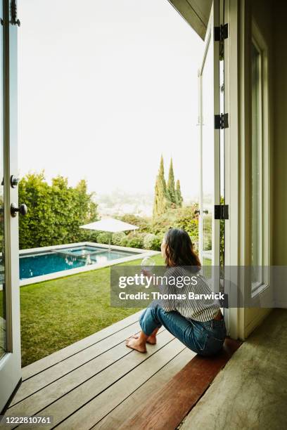 woman enjoying glass of wine while looking out over pool in backyard - true luxury stock-fotos und bilder