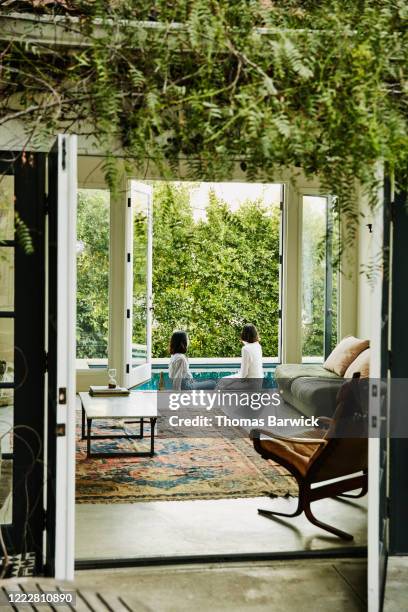 view through living room of female friends sitting on deck overlooking backyard pool - backyard deck stockfoto's en -beelden