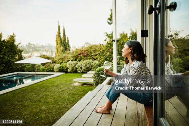 smiling woman enjoying glass of wine while watching sunset from backyard - casual mode stock-fotos und bilder