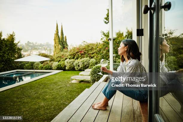 smiling woman enjoying glass of wine while watching sunset from backyard - indulgence photos et images de collection