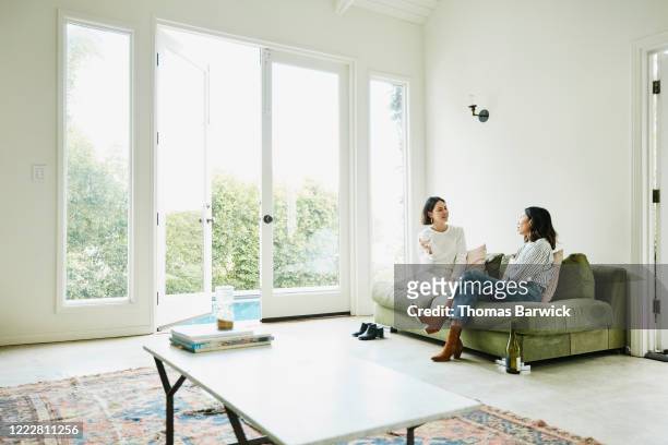female friends relaxing in living room drinking wine - friends talking living room stock-fotos und bilder