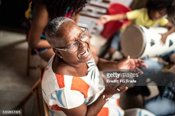 portret van grootmoeder die muziek thuis speelt - met familie op achtergrond - samba stockfoto's en -beelden