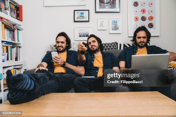 multi-tasking man doet veel activiteiten als hij in quarantaine - man watching tv on couch stockfoto's en -beelden