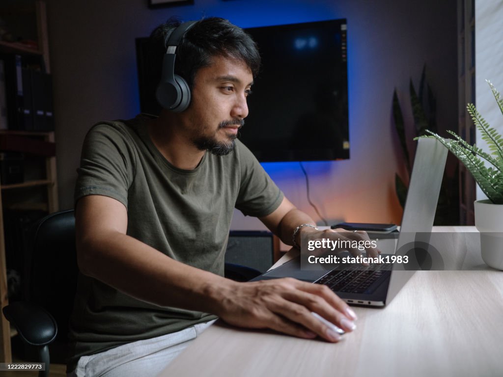 Millennial man playing computer game on laptop at home.