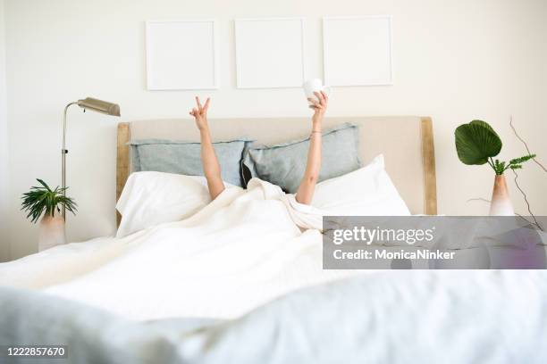 手にコーヒーマグカップでベッドで目を覚ますヒスパニックの成熟した女性 - headboard ストックフォトと画像