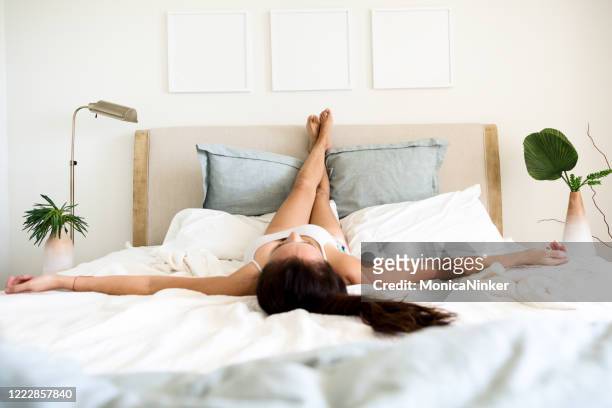 a woman in lying on bed with legs up towards headboard - feet up stock pictures, royalty-free photos & images