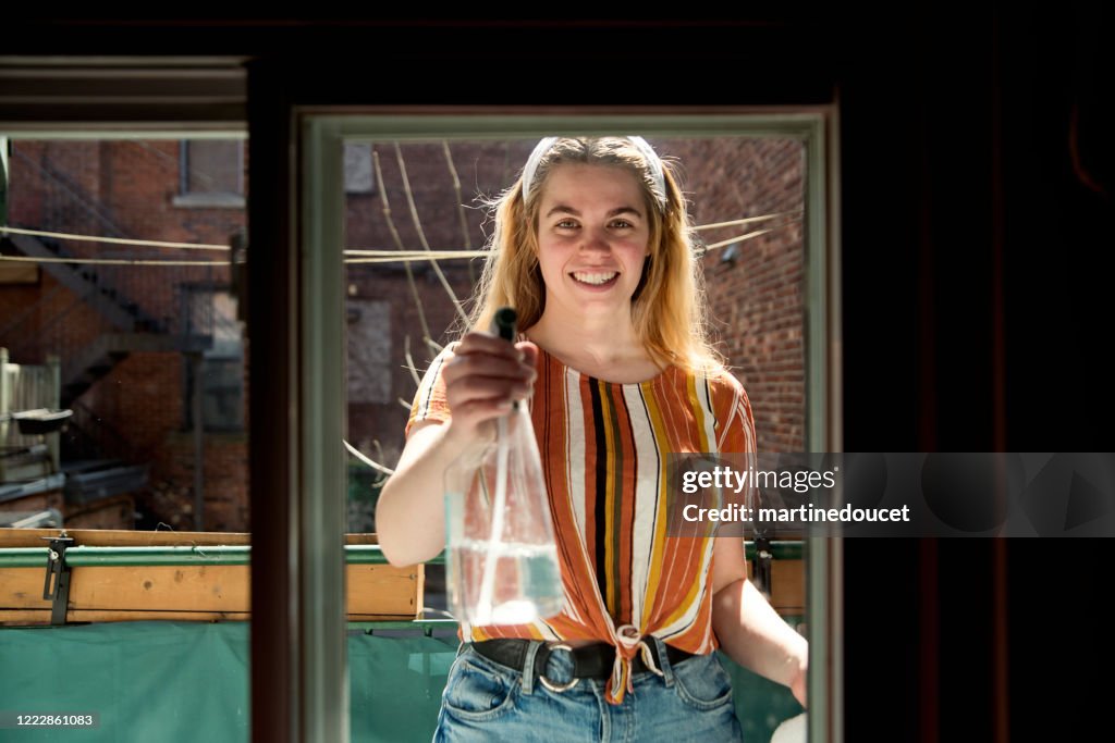 Millenial mujer limpieza ventana en el balcón de la ciudad en primavera.