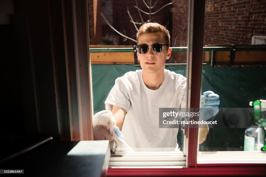 Finestra di pulizia dell'uomo millenial sul balcone della città in primavera.