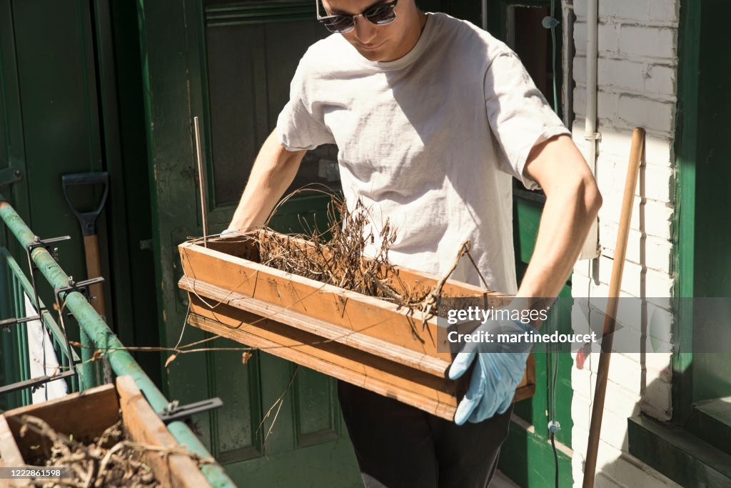 Millenial mens die stadsbalkon in de lente schoonmaakt.