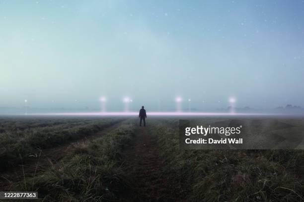 a science fiction concept. a man standing in a field back to camera looking into the sky, with glowing ufo orbs on the horizon - flying saucer stock pictures, royalty-free photos & images