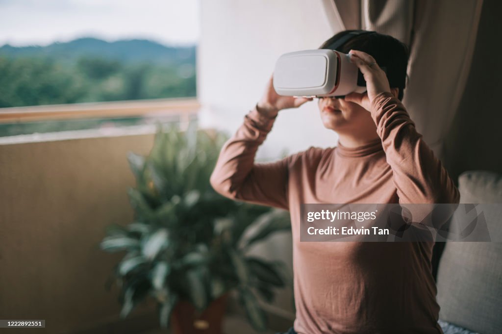 An asian chinese mid adult woman playing games enjoying VR virtual reality online using VR google in living room