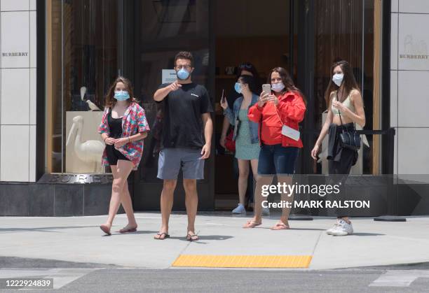 People wearing facemasks stand outside a Burberry store as shoppers return to the streets of iconic Rodeo Drive as the luxury goods stores reopen...