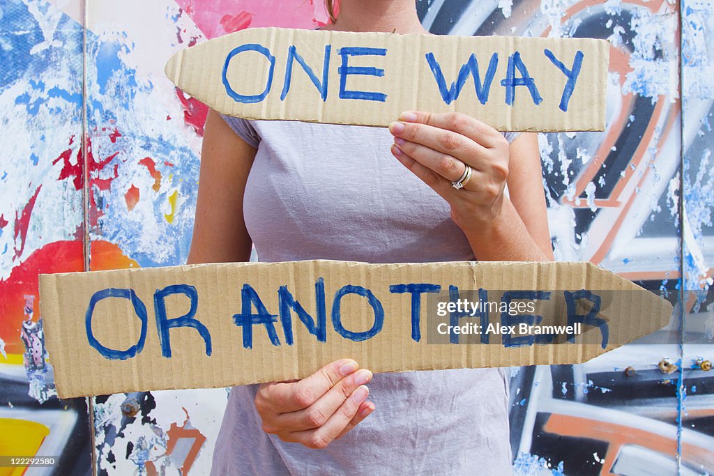 Woman holding conflicting direction signs