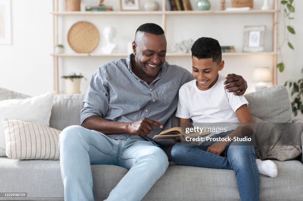 Mogen afroamerikansk man läser bok med sitt barnbarn hemma