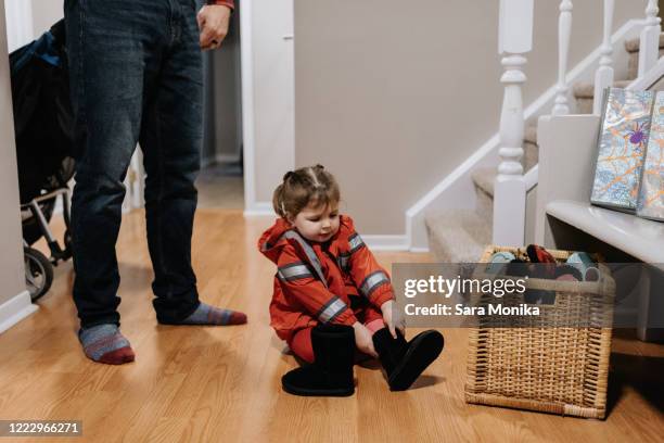 a little girl dressed as a firefighter sitting on a wooden floor pulling on black boots. - firefighter boot stock pictures, royalty-free photos & images