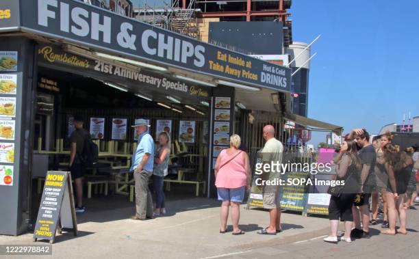 People queue outside a fish and chips takeaway on the hottest day of the year. People head to the beach at the popular seaside resort of Skegness as...