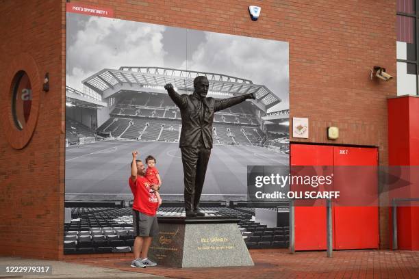 Liverpool fans pose for a photograph beside the statue of former manager Bill Shankly as supporters celebrate Liverpool sealing the Premier League...