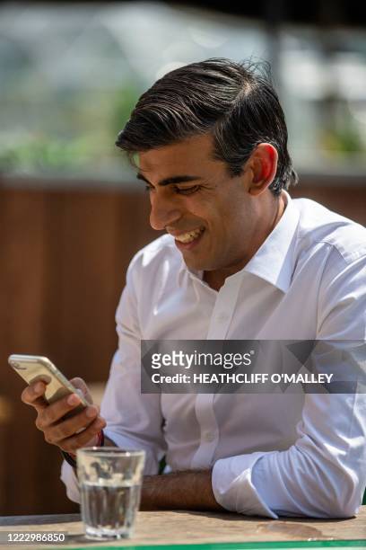 Britain's Chancellor of the Exchequer Rishi Sunak uses his smartphone as he visits Pizza Pilgrims in West India Quay, London Docklands on June 26,...