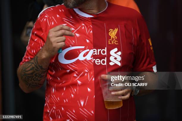 Liverpool fan wears a half-an-half Liverpool shirt featuring 1990 and 2020 symbolising the 30 years between Premier League victories, as he drinks a...