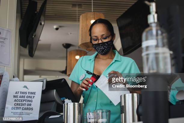 An employee wearing a protective mask stands behind a sign notifying customers that credit and debit cards are the only accepted form of payment at a...