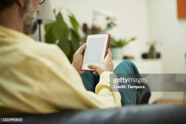 one mid adult man reading on an e-reader seen from behind. - e reader stock pictures, royalty-free photos & images