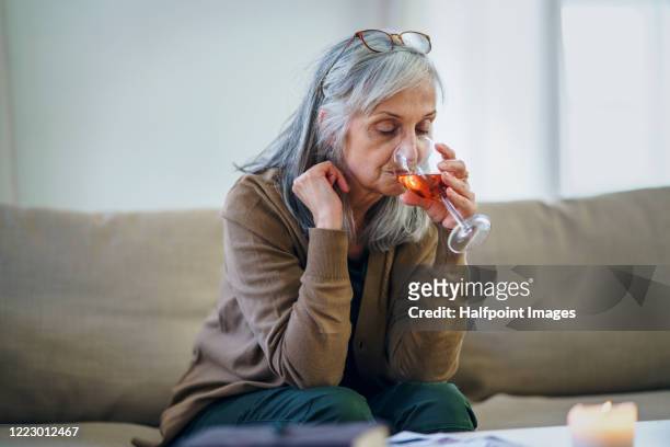 sad and depressed woman sitting indoors on sofa, drinking wine. - alcohol abuse stock pictures, royalty-free photos & images