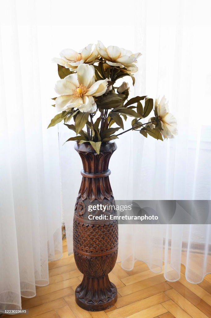 Wooden carved vase with artifical flowers in daylight.