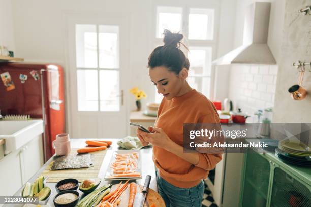 millennial frau überprüfen rezepte online - frau kochen stock-fotos und bilder