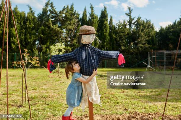 junges mädchen umarmt vogelscheuche in community garden - scarecrow stock-fotos und bilder