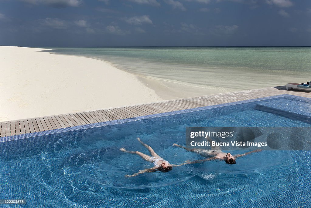 Couple floating in infinity pool on beach