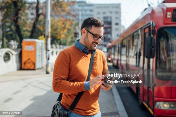 online-geschäft: glücklicher geschäftsmann arbeitet mit seinem smartphone auf der straße - orange bus stock-fotos und bilder