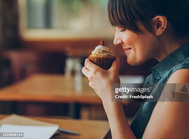 having a sweet tooth: happy woman enjoying the aroma of a delicious pumpkin spice cupcake - person holding cupcake stock pictures, royalty-free photos & images