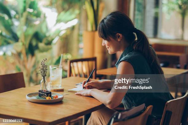 happy young woman writing notes in her notebook while sitting at a cafe - writing stock pictures, royalty-free photos & images