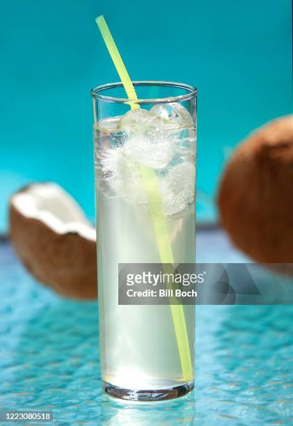 glass of iced coconut water with a cracked coconut shell behind it, on a outside patio table by a swimming pool-part of a series - coconut water stock pictures, royalty-free photos & images