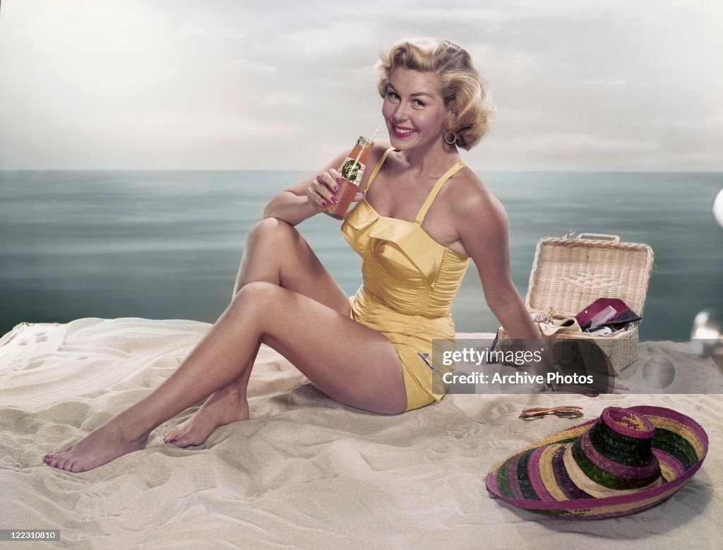 Young woman holding cold drink bottle on beach smiling, portrait