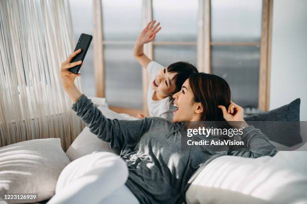 young asian mother and little daughter video conferencing with smartphone to connect with their friends and family at home - chinese family taking photo at home stock pictures, royalty-free photos & images