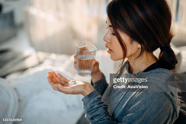 giovane donna asiatica seduta a letto e malata, che prende medicine in mano con un bicchiere d'acqua - diarrhoea foto e immagini stock