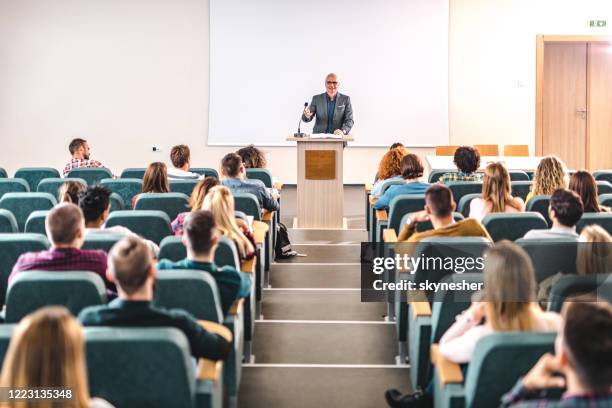 glücklicher reifer professor, der einen vortrag vor der projektionsfläche im hörsaal hält. - lecture theatre stock-fotos und bilder