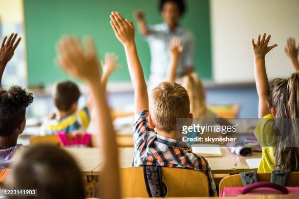 achtermening van elementaire studenten die hun handen op een klasse opheffen. - armen omhoog stockfoto's en -beelden