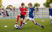 Kids Football Players Kicking Ball on Soccer Field. Sports Soccer Horizontal Background. Spectators on Stadium in the Background. Youth Junior Athletes in Red and Blue Soccer Shirts. Sports Education
