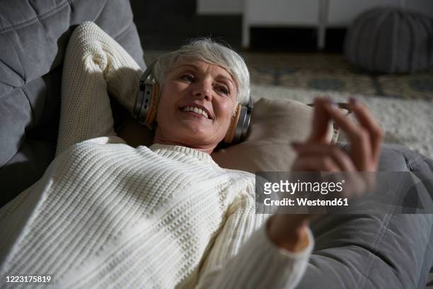 portrait of senior woman relaxing on couch listening music with headphones - met de vingers knippen stockfoto's en -beelden