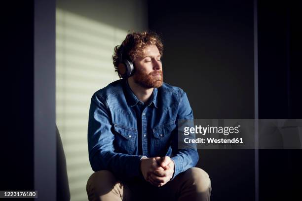 relaxed casual businessman sitting down listening to music with headphones - listening imagens e fotografias de stock