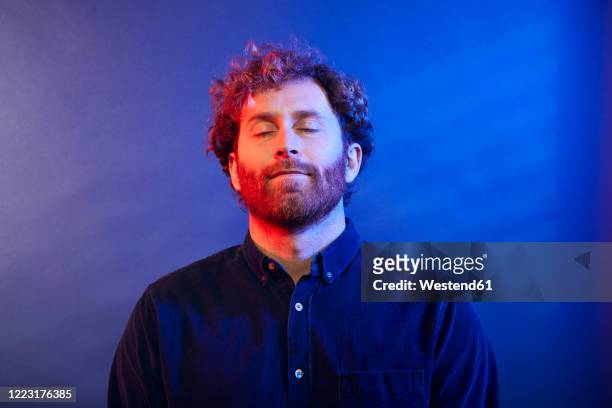 portrait of a man with closed eyes at a blue wall - man smiling eyes closed stock pictures, royalty-free photos & images