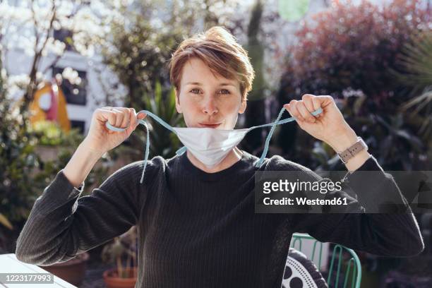 woman siting in garden, removing face mask - entfernen stock-fotos und bilder