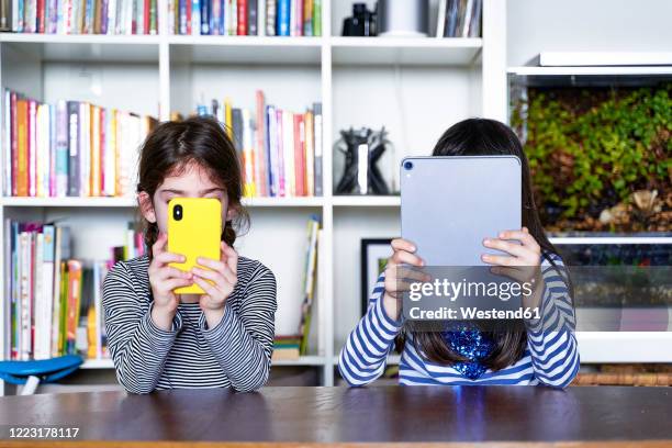 two sisters sitting side by side at table in the living room using electronic devices - tutorial stock pictures, royalty-free photos & images