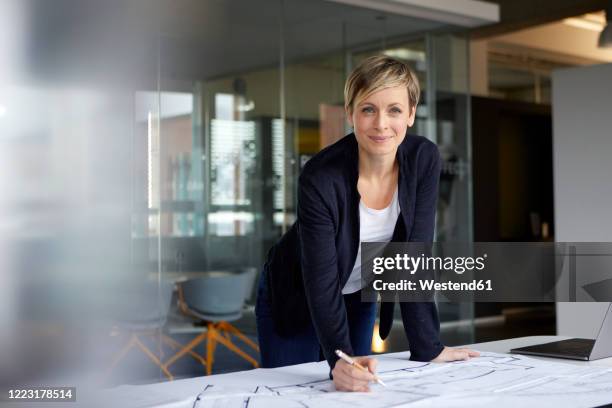 portrait of smiling woman working on construction plan in office - content development stock pictures, royalty-free photos & images