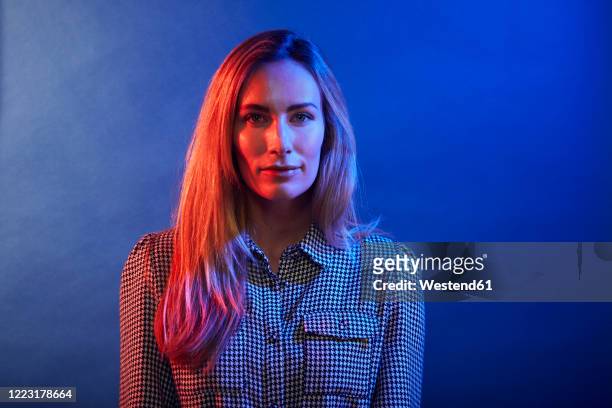 portrait of woman in front of a blue wall - licht stock-fotos und bilder