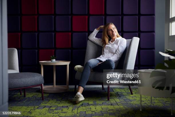 smiling woman sitting in armchair in modern lounge - armchair imagens e fotografias de stock