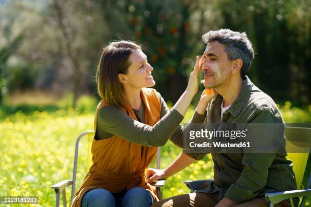 young woman putting sunscreen on her boyfriend in the field - putting lotion stock pictures, royalty-free photos & images